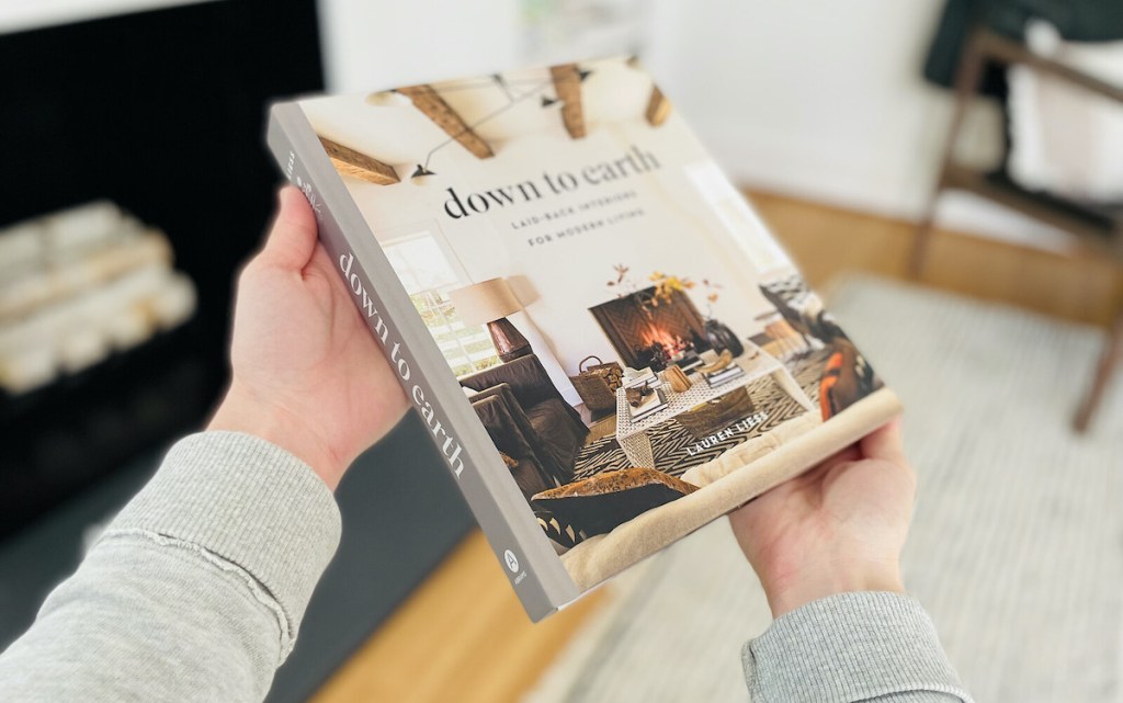 hands holding out down to earth coffee table book in front of fireplace