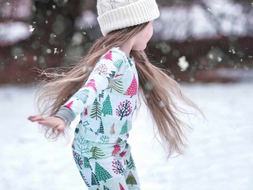 little girl outside in snow in pajamas and hat