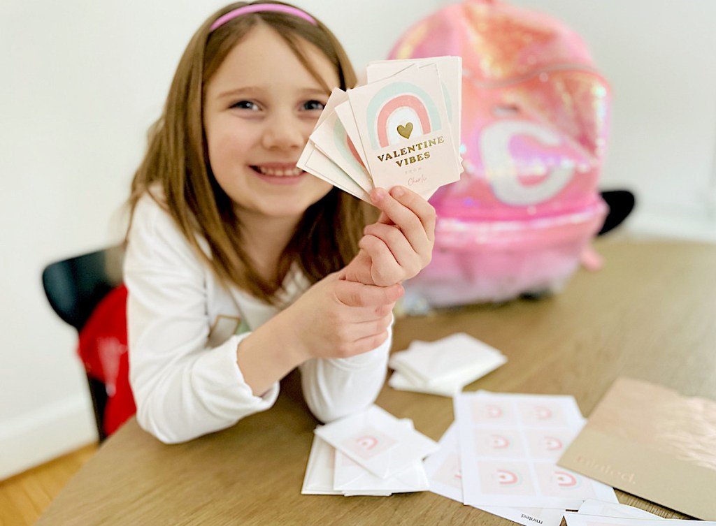 girl holding stack of rainbow minted valentines day cards sitting at table