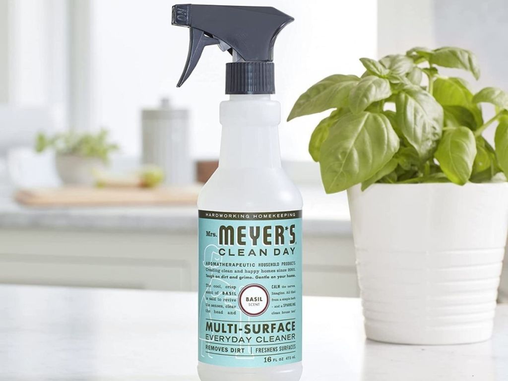 a bottle of mrs meyers clean day basil all purpose cleaning spray on a kitchen counter next to a basil plant in a white pot