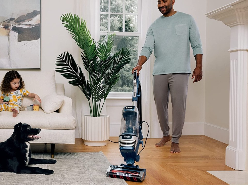 man vacuuming in room with child and dog