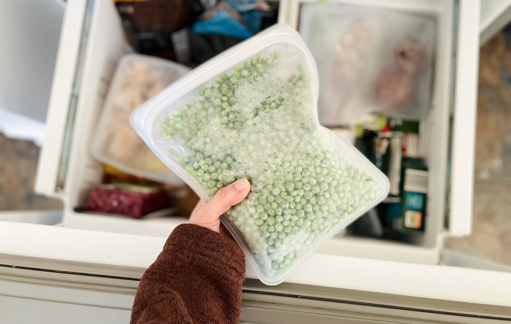 hand holding a full clear bag of frozen peas over freezer