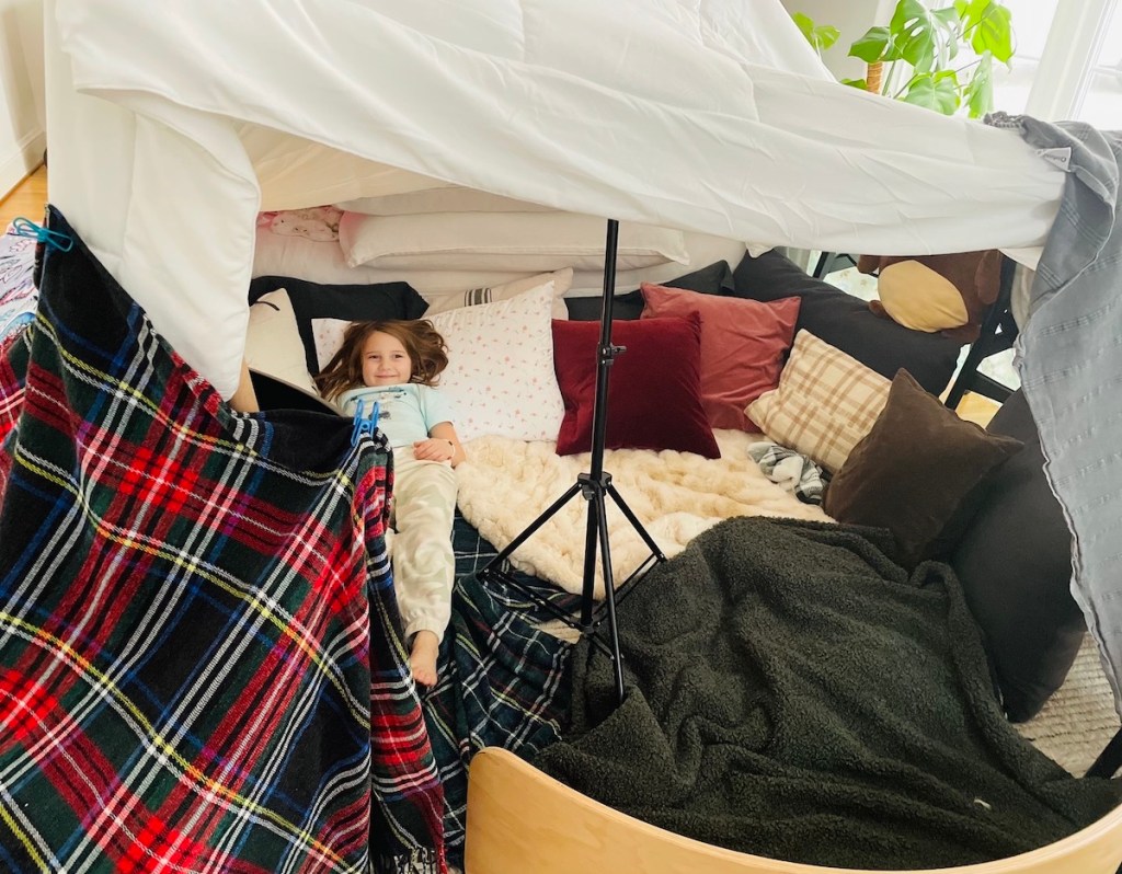 girl inside throw blanket tent with tons of pillows 