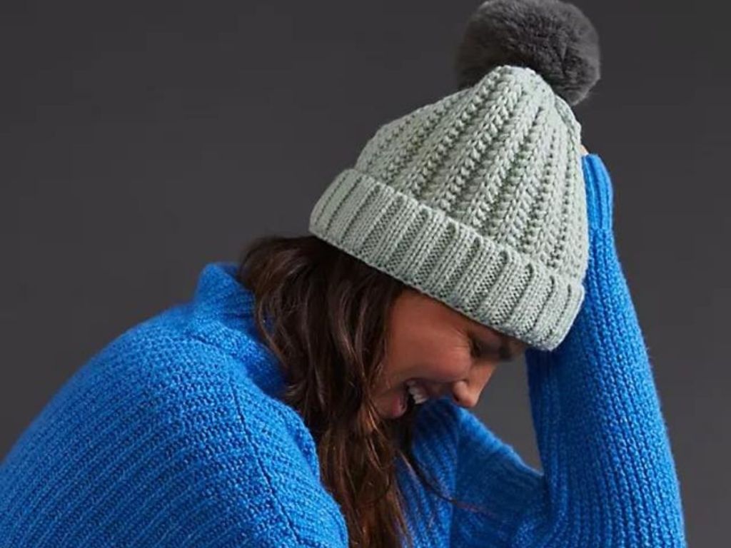 woman wearing blue sweater and gray pom beanie