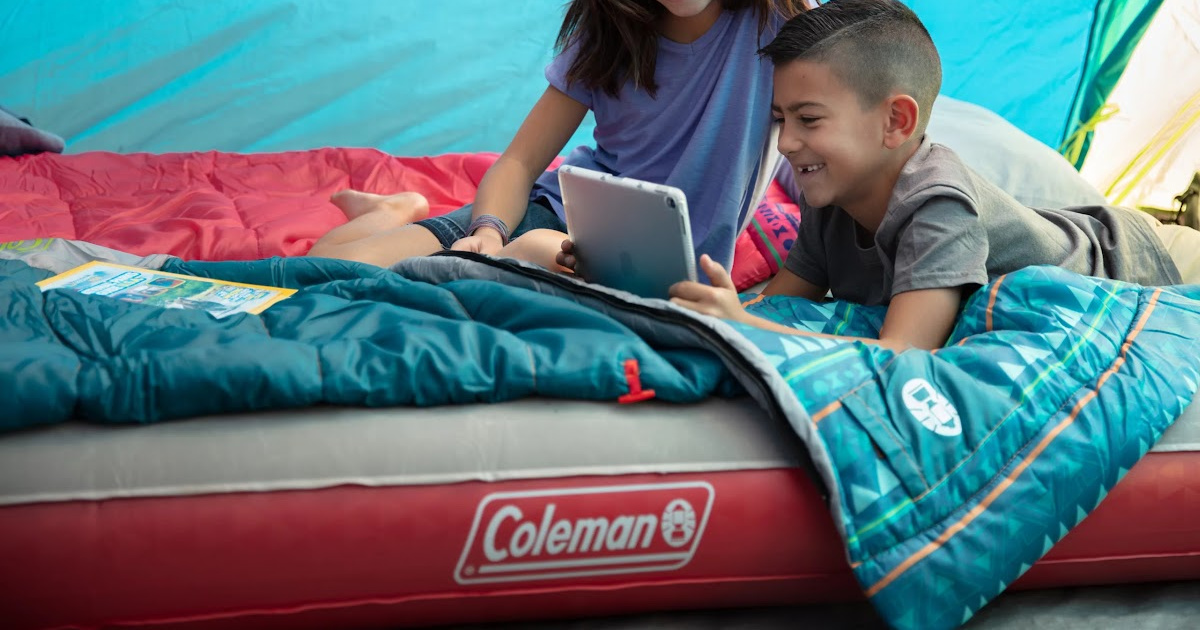 boy and girl sitting on air mattress and sleeping bags in tent