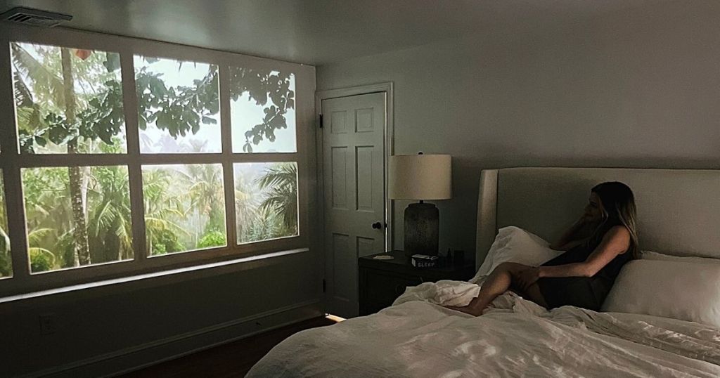 tropical window projected onto bedroom wall with woman laying in bed looking at it
