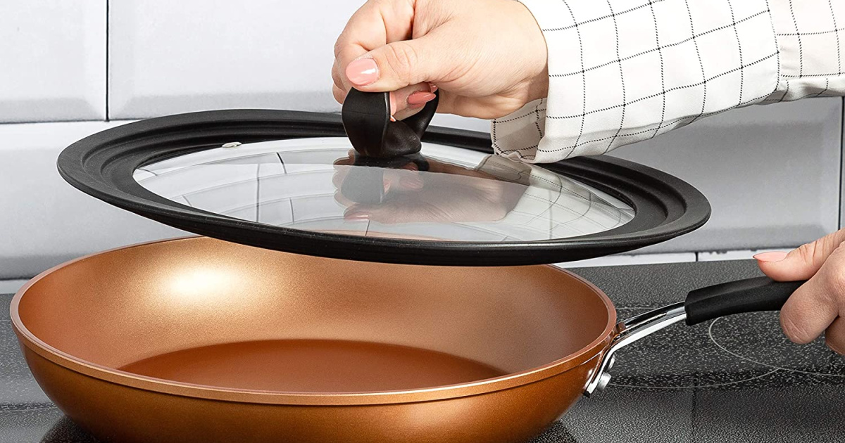 hand lifting a glass lid off a copper pan