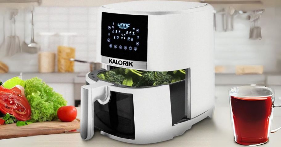 white air fryer with basket open on kitchen counter with food and drink around it