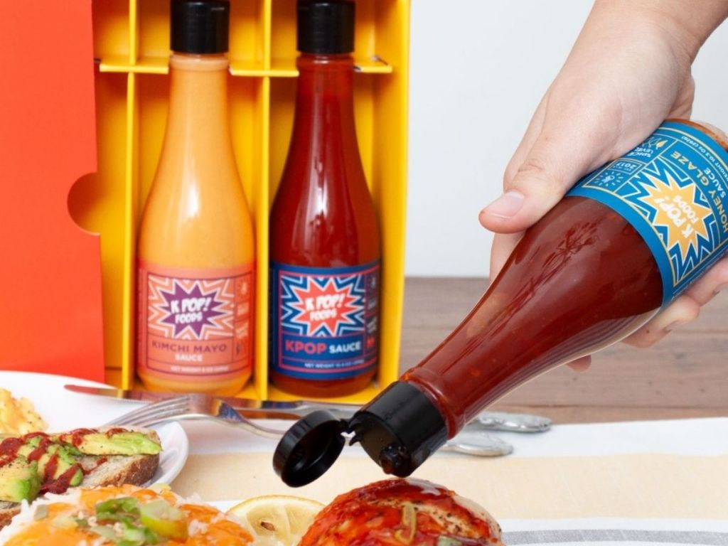KPOP Foods Sauce getting poured on food with a couple bottles in the background