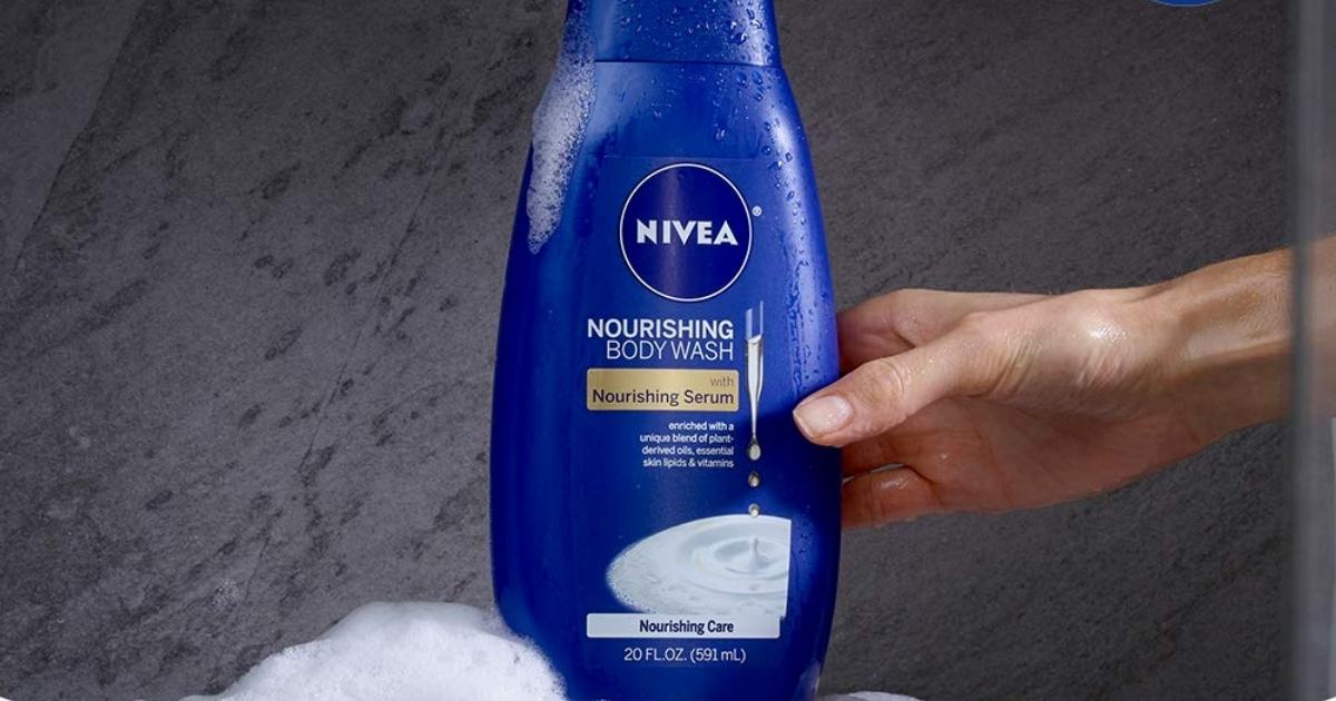 hand holding a bottle of nivea body wash against a slate wall with some lather under it