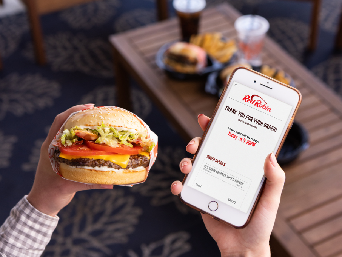hand holding burger and cell phone displaying red robin coupons & royalty rewards