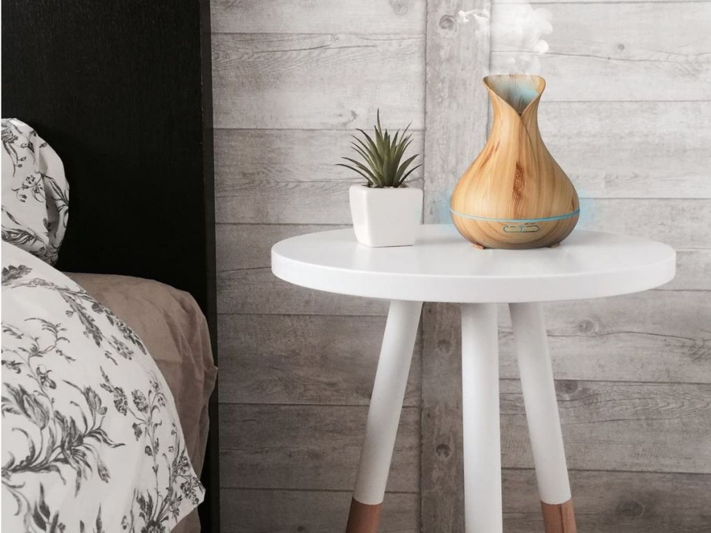light wood essential oils diffuser on white end table with tiny plant next to it