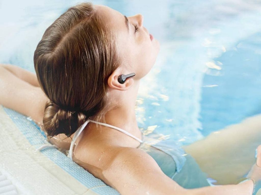 woman sitting in pool wearing black Taotronics earbud