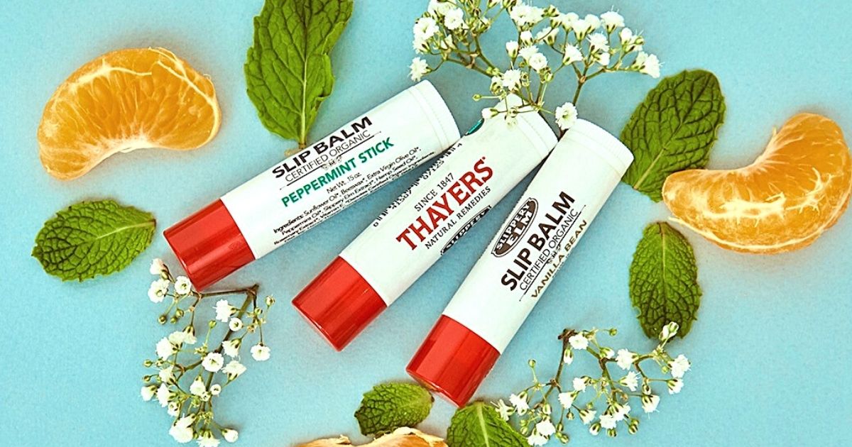 three Thayers organic lip balms laid out with various flowers, herbs, and fruit slices