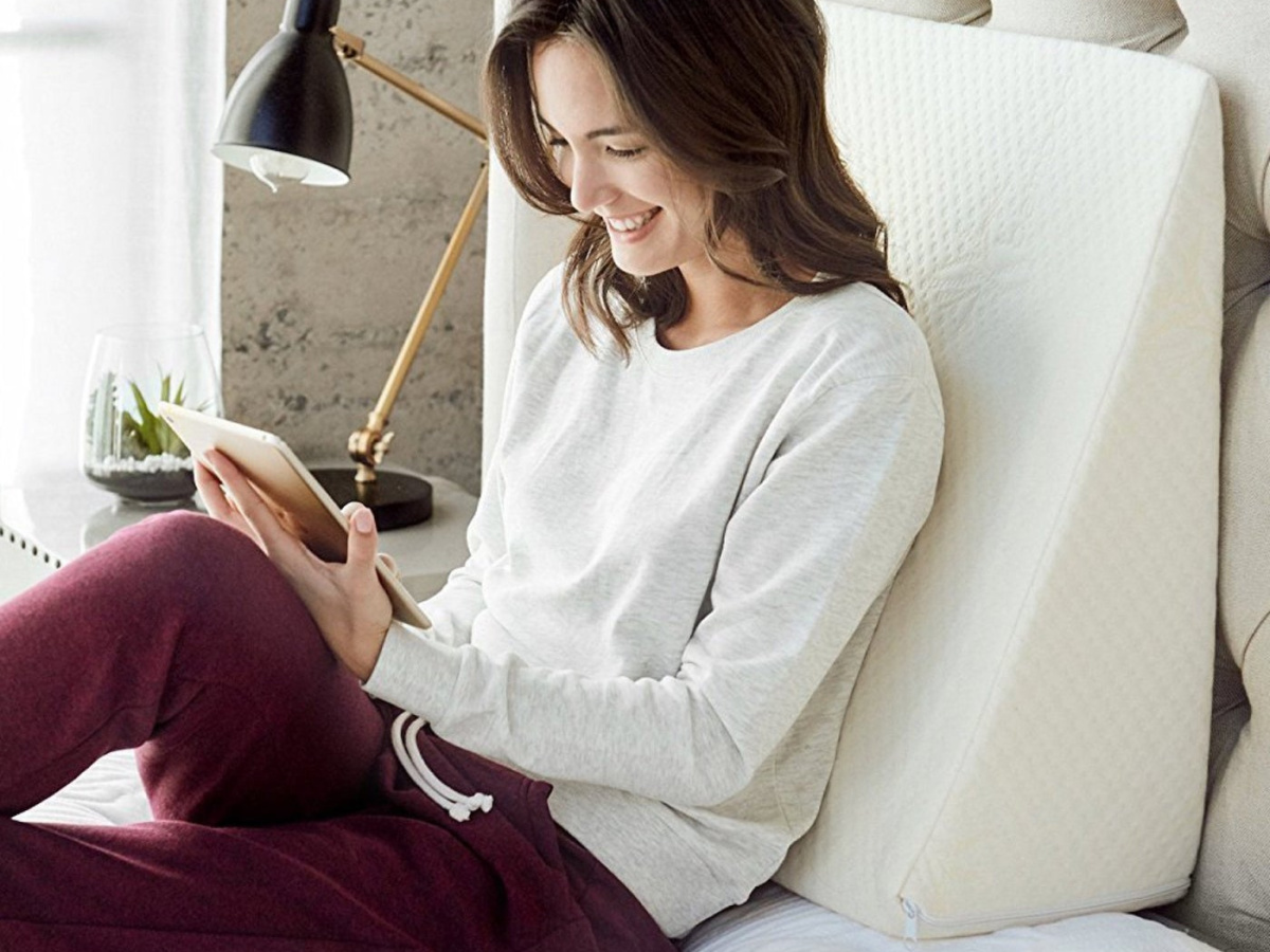 woman sitting in bed leaning against foam wedge pillow, and using tablet