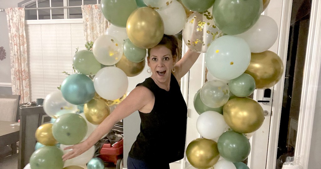 woman holding up gold white and green balloon arch