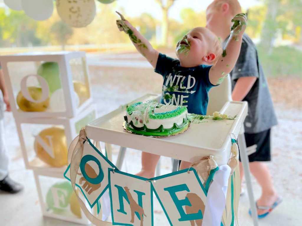 baby boy sitting in highchair with smash cake and party decorations