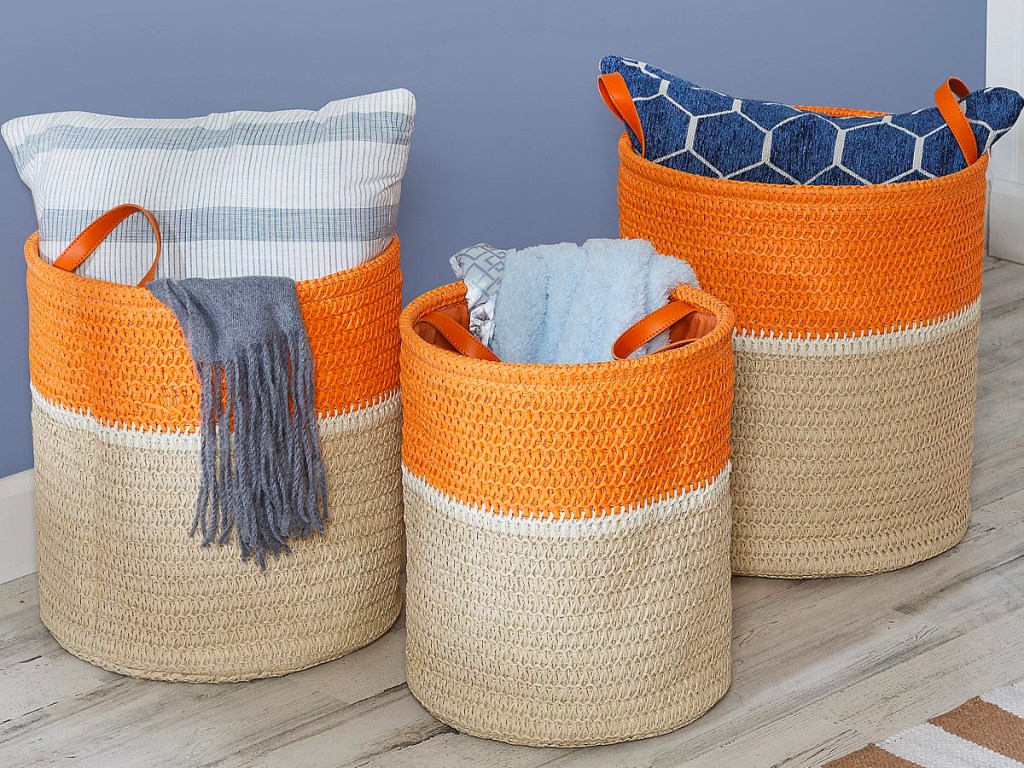 three beige and orange baskets with pillows and blankets in them