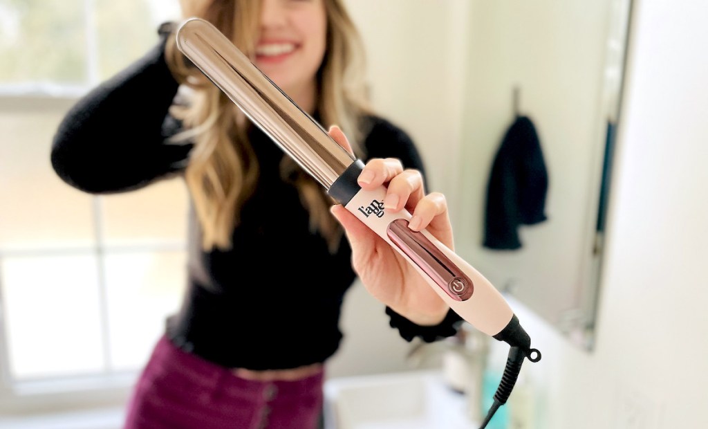 woman holding curling wand in bathroom smiling