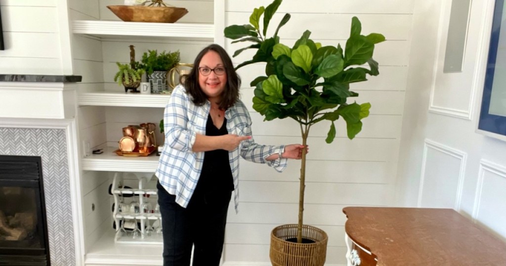 woman standing next to tall fiddle leaf fig tree in corner of white living room