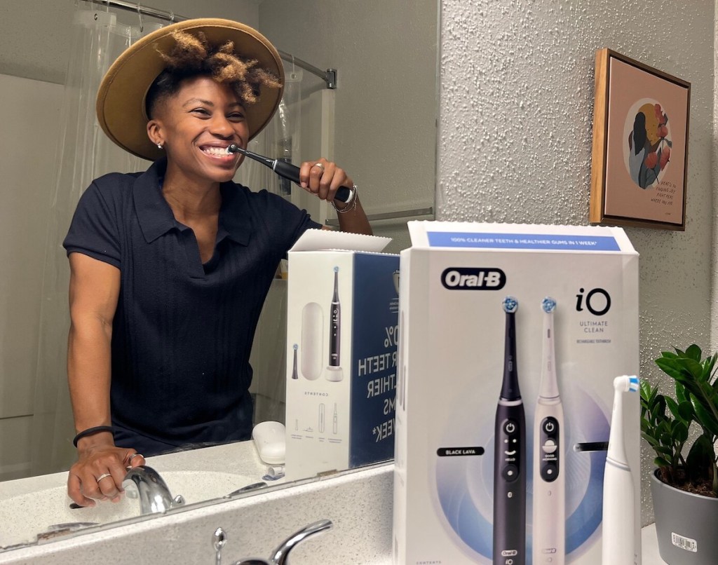 woman brushing teeth in mirror smiling with oral b toothbrush costco
