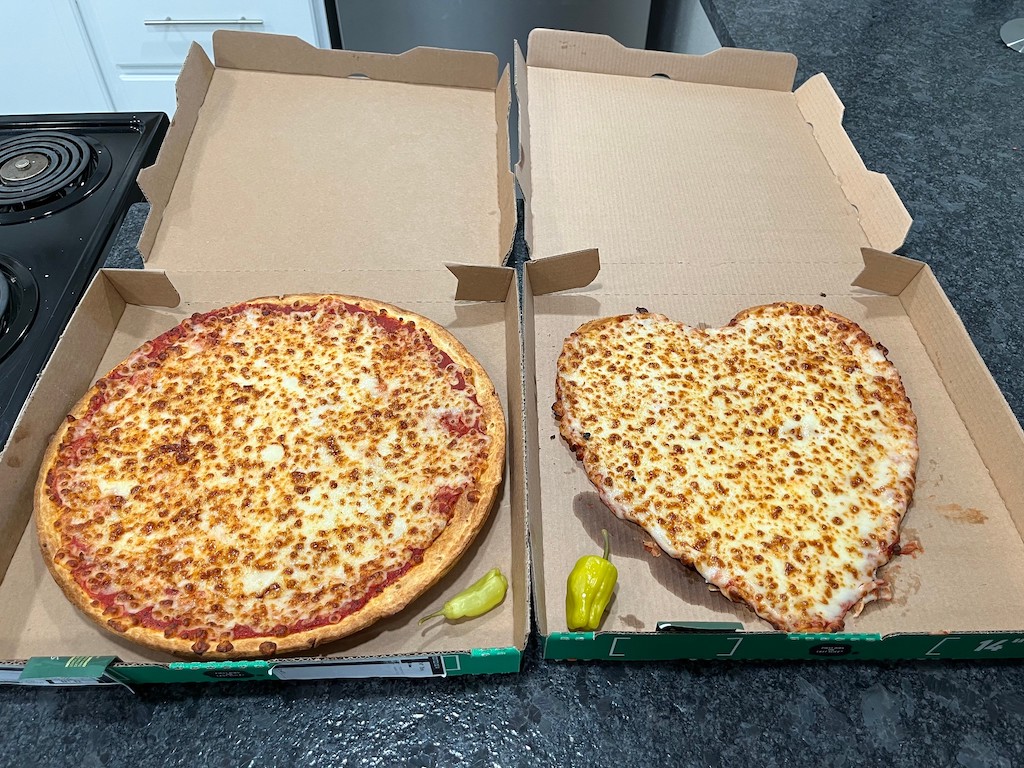 two cheese pizza in boxes - one is heart shape 
