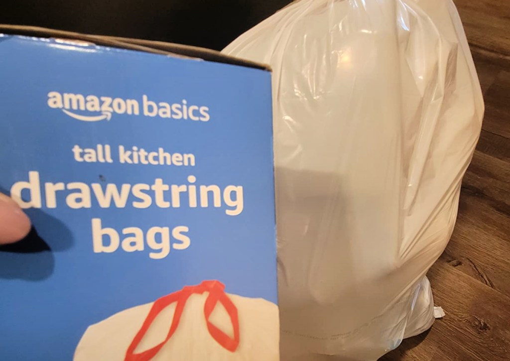 person holding box of Amazon Basics Tall Kitchen Drawstring trash bags 