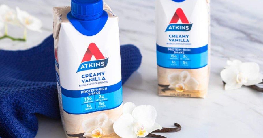 Atkins Creamy Vanilla Shakes beside of vanilla beans and flowers