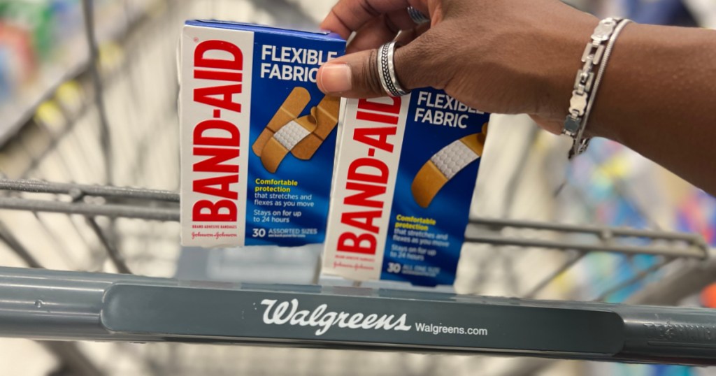 ręka trzymająca dwa pudełka bandaży plastrowych w wózku sklepowym