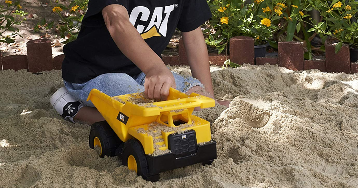 boy playing with yellow dump truck in sand