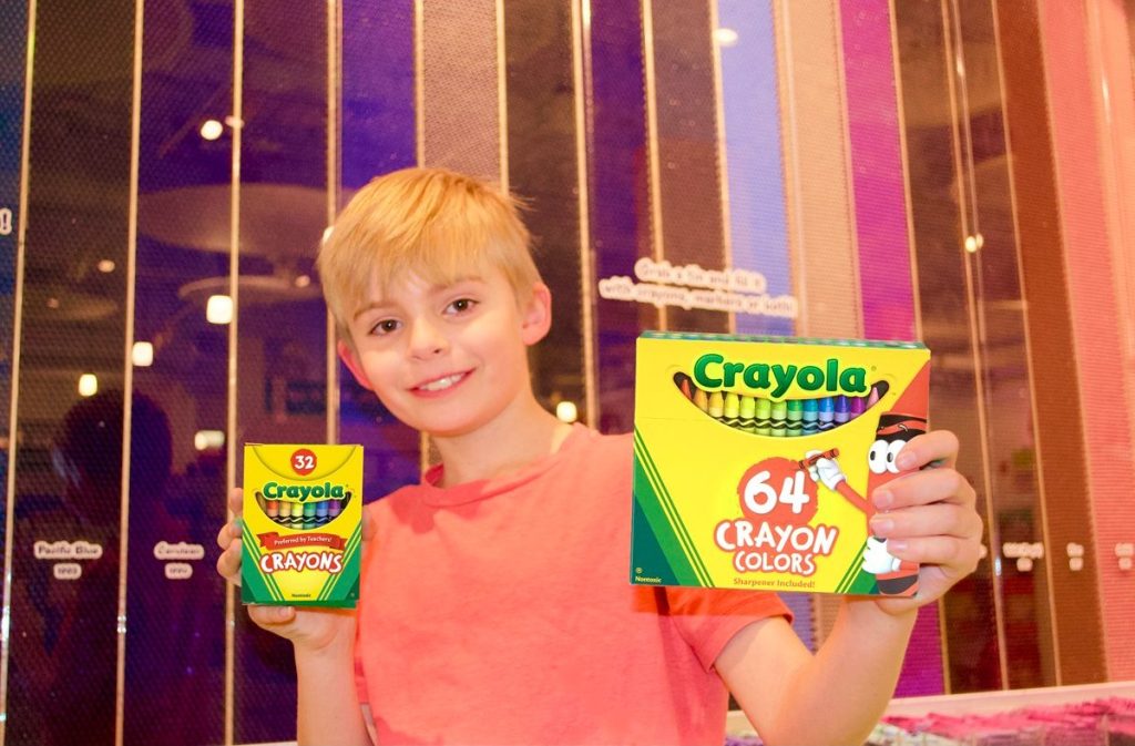 boy smiling and holding two boxes of crayons
