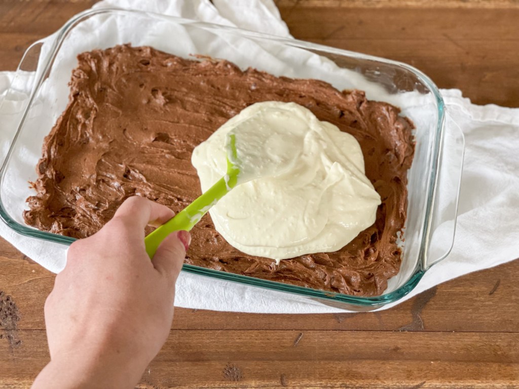 adding cream cheese mixture to brownie batter in a baking dish