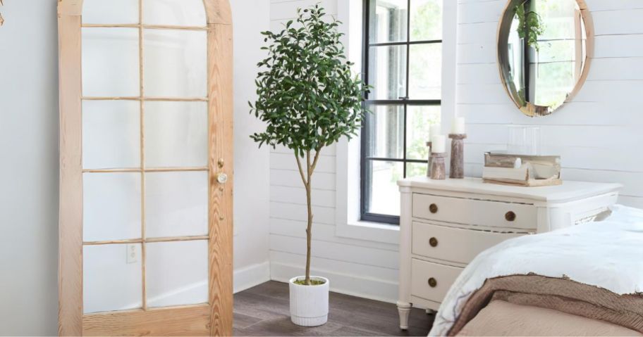 artificial olive tree in a white planter shown in corner in bedroom