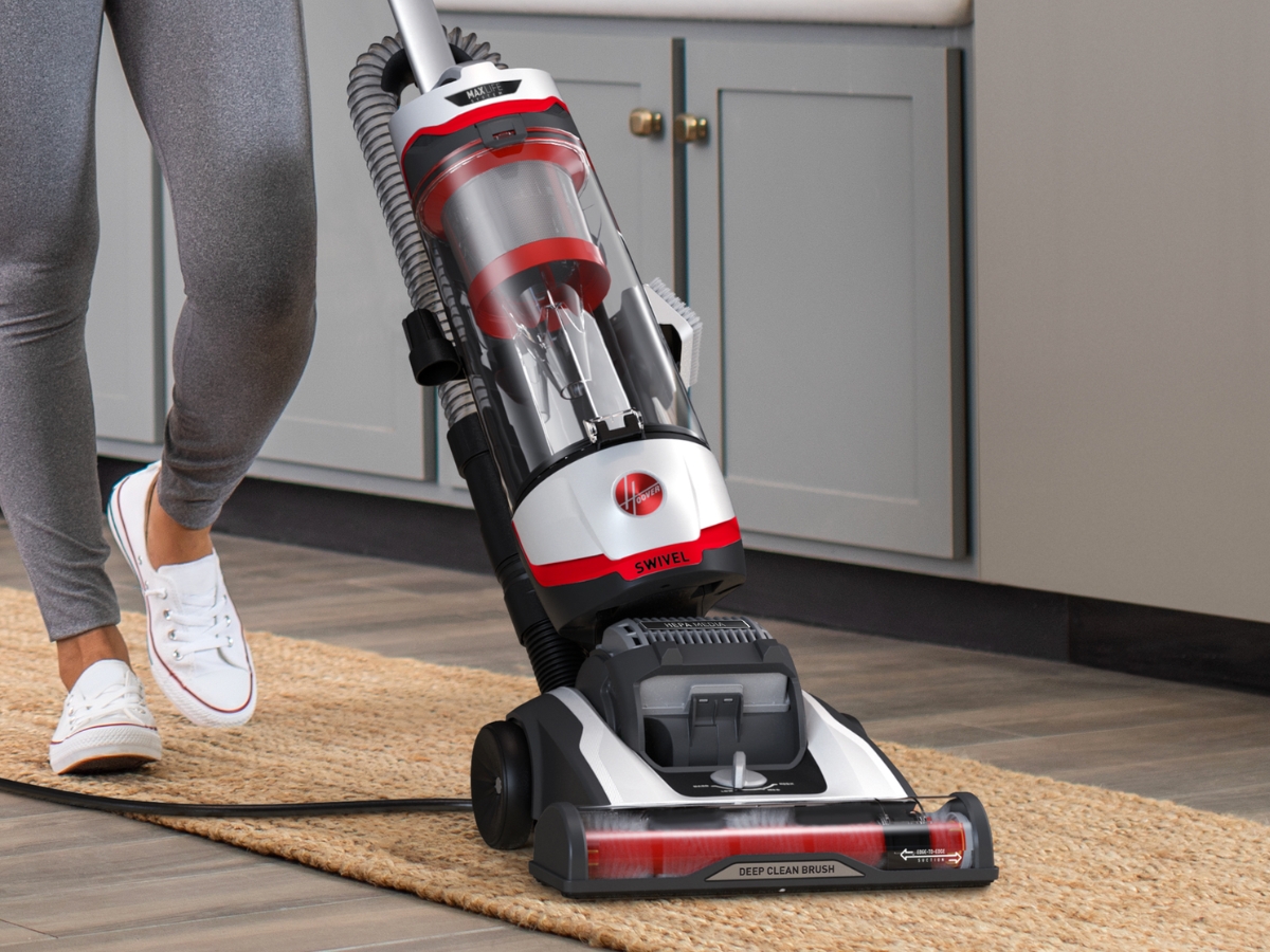 woman pushing a hoover vacuum across a runner rug in a kitchen near cabinets