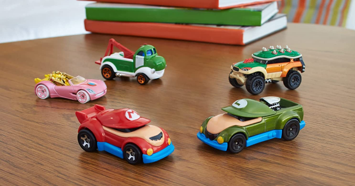 five Hot Wheels Super Mario cars on a table near a stack of books