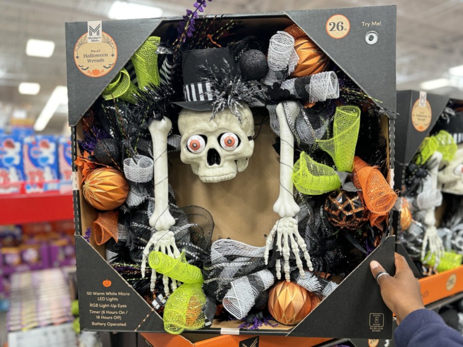 hand holding up a black halloween wreath with skeleton in center