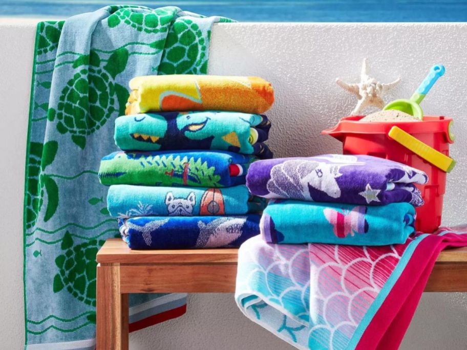 Stack of folded beach towels on a bench and a towel draped over a wall behind the bench