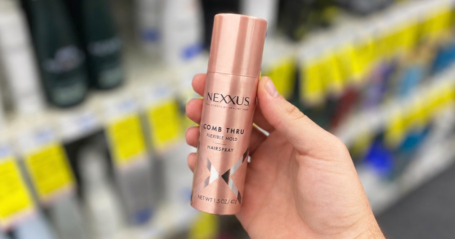 hand holding a mini pink bottle of nexxus hair spray in store