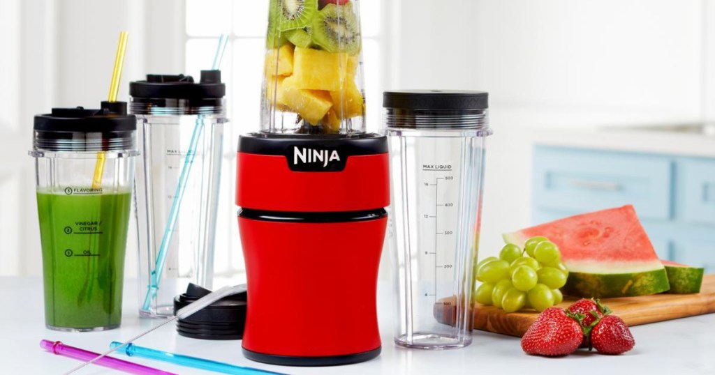 Red Ninja blender with cups and fruit on counter