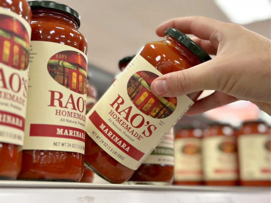 A hand taking a jar of Rao's marinara off a shelf.