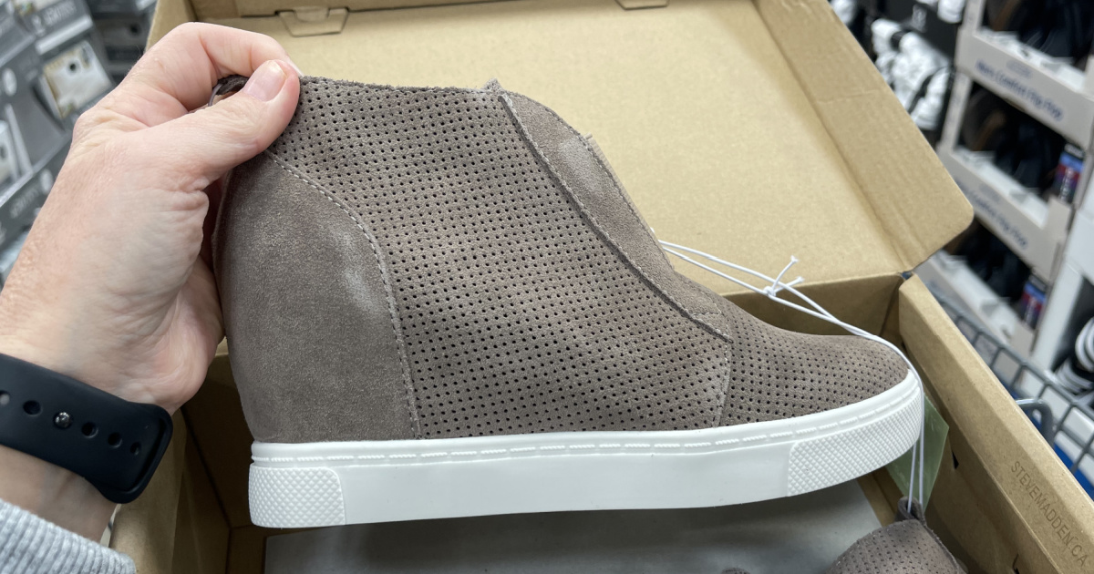 woman's hand holding taupe wedge sneaker in store