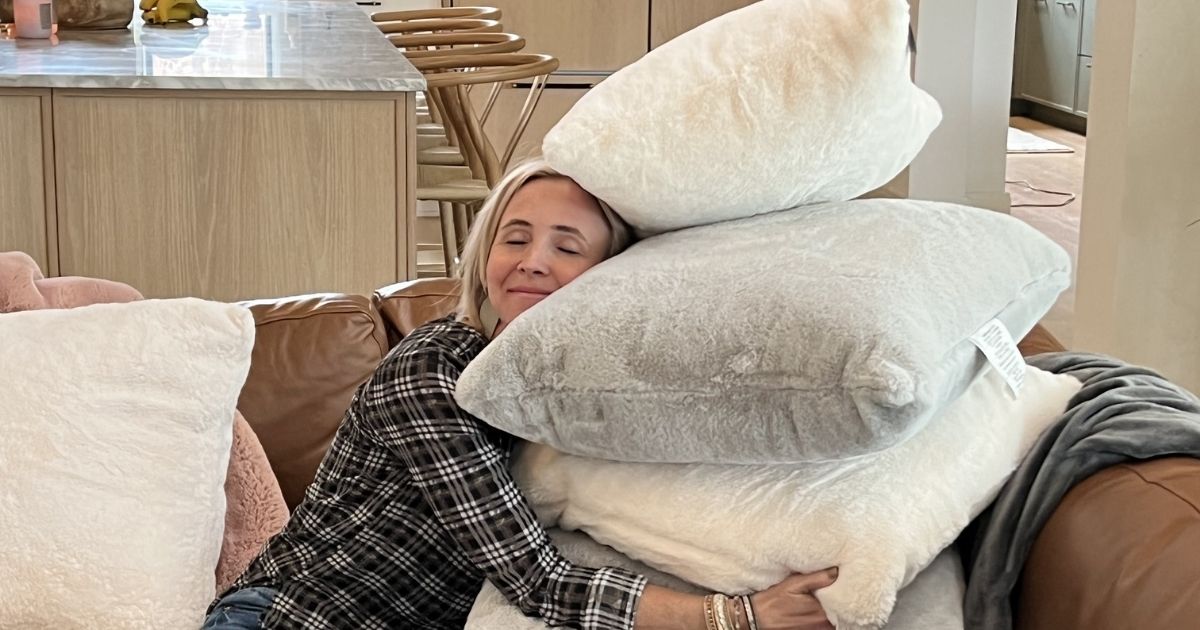 women sitting on couch hugging a stack of pillows