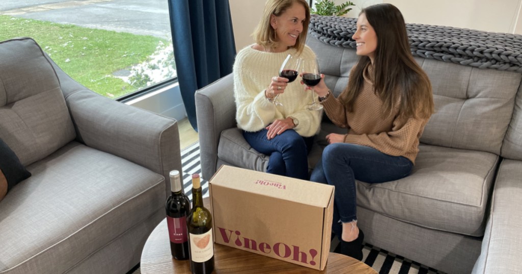 two women sitting on couch with glasses of wine