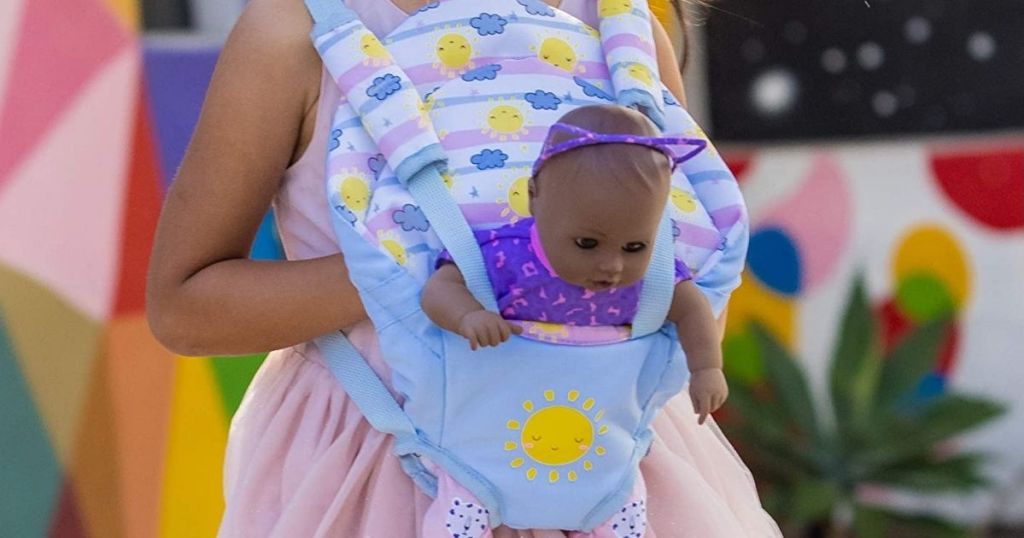 little girl holding baby doll in toy carrier