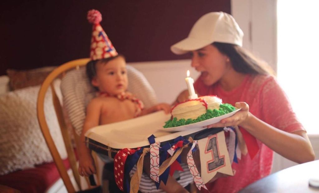 woman holding cake in front of baby in highchair