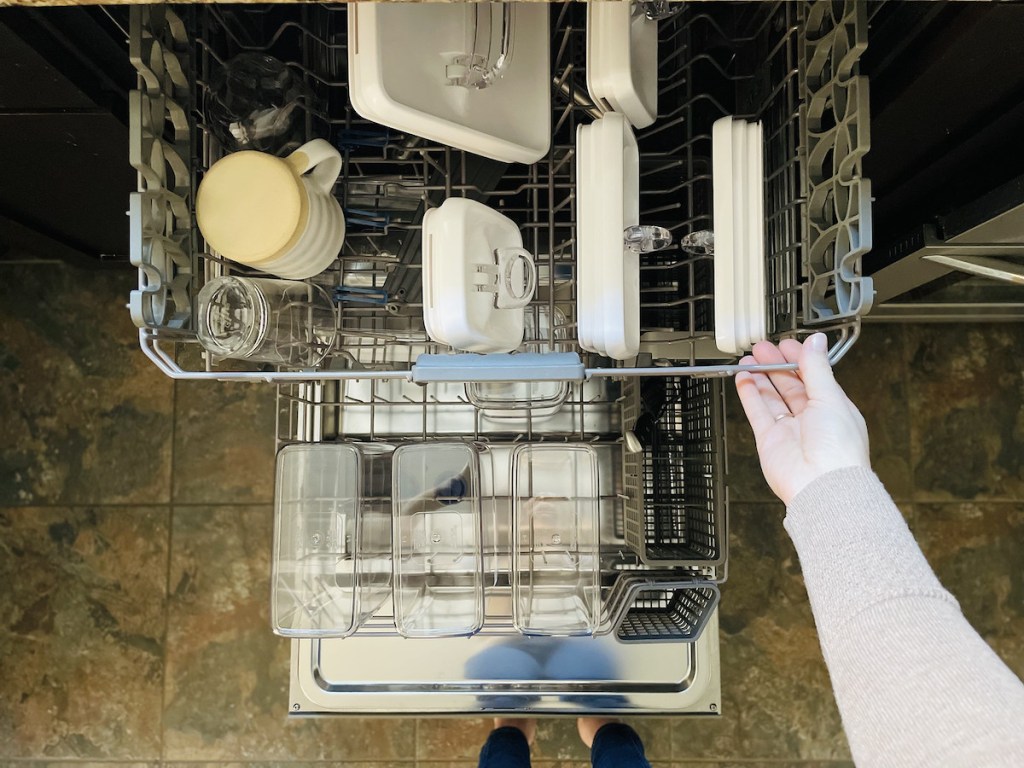 hand pulling out top drawer of dishwasher with food storage containers inside