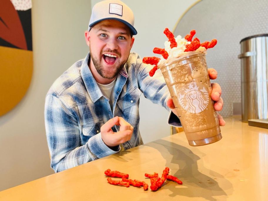 man holding starbucks frappuccino with whipped cream and flamin hot cheetos