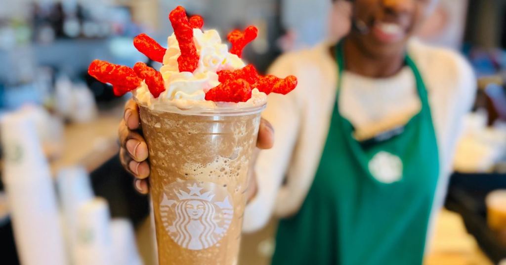 barista holding starbucks frappuccino with whipped cream and flamin hot cheetos