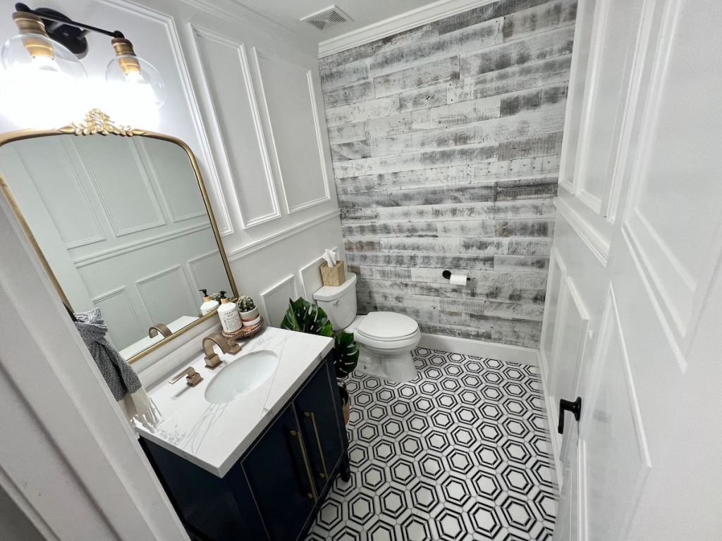 zoomed out view of new renovated half bath with gold fixtures and black and white hexagon floor