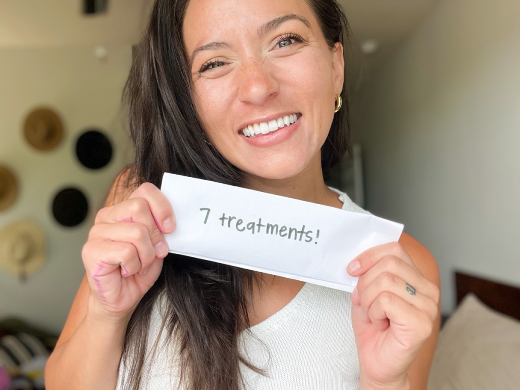 smiling woman holding a piece of paper that says 7 treatments after using lumineux teeth whitening kit items